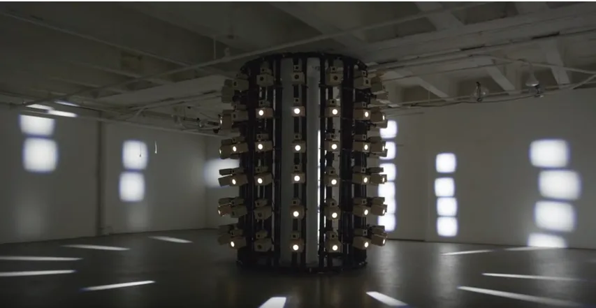 A tall cylindrical installation surrounded by rectangular projections of light in panopticon