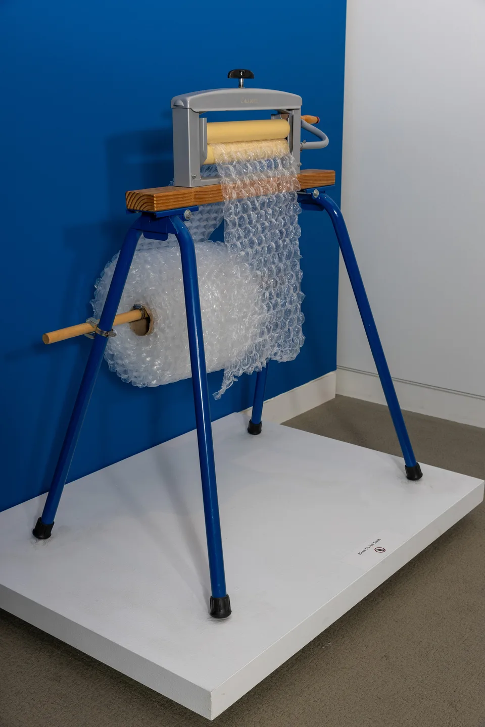 A hand-cranked wringer on blue metal legs feeds a roll of bubble wrap.