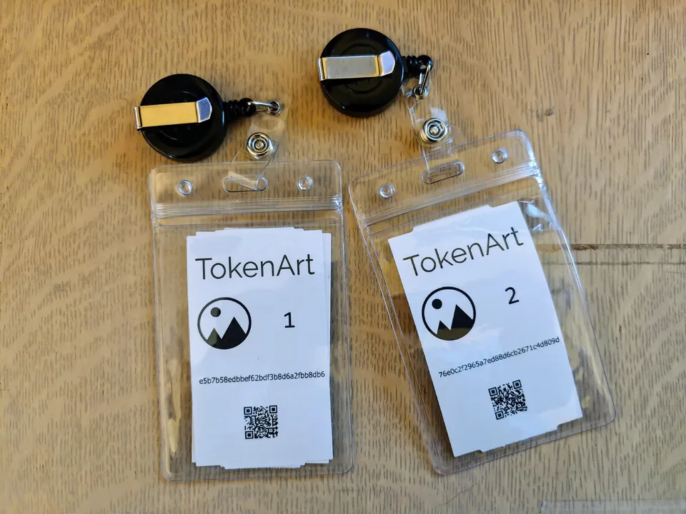 Two numbered TokenArt badges with QR codes and retractable clips lying on a wooden surface