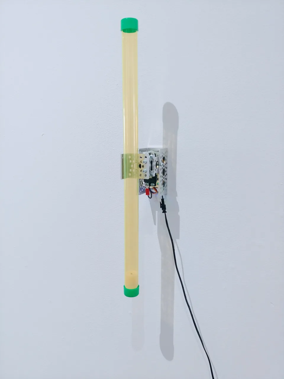 A long yellow tube with green end caps is attached at its middle to a wall-mounted motorized mechanism.