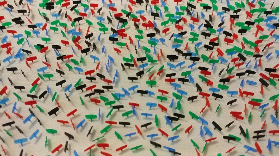 A close view of small red, blue, green, and black tagging attachments projecting from a white canvas
