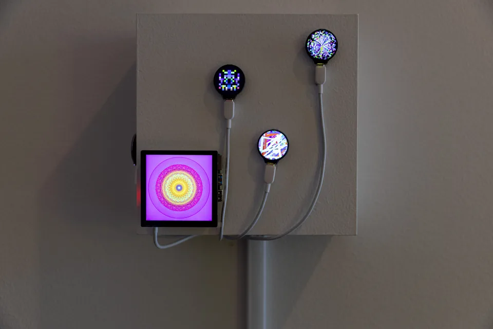 A square screen with concentric colored patterns and three small circular displays mounted together on a wall.