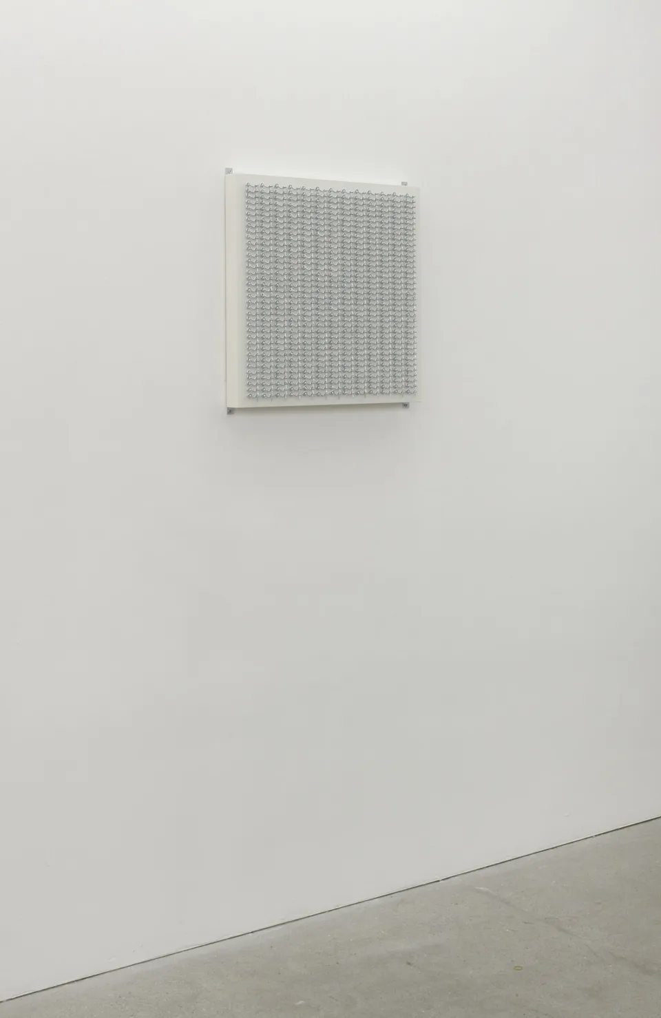 A panel of small metal hooks installed on a gallery wall