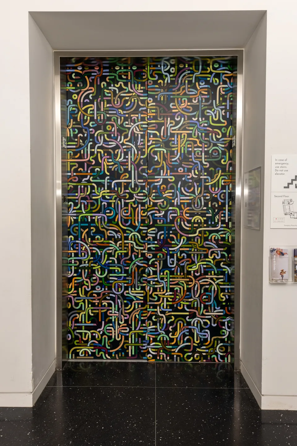 Elevator doors covered with multicolored looping lines on a dark background.