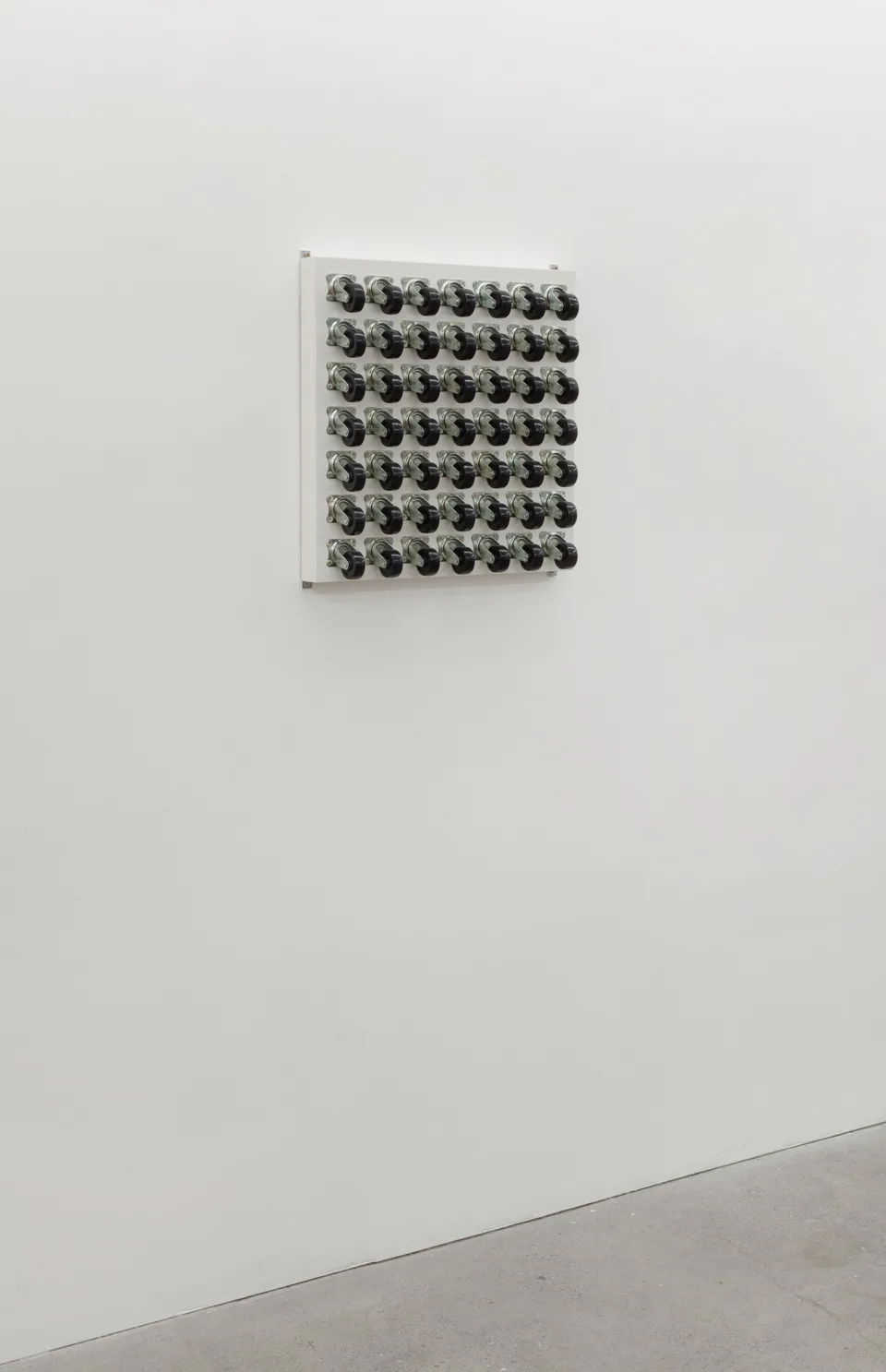 A grid of caster wheels installed on a gallery wall