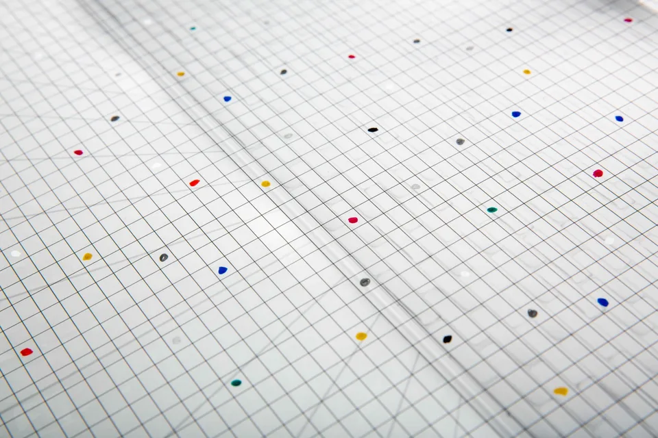 Angled detail of the fine black grid and small colored dots over the image of a white room.