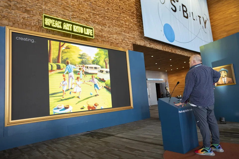 A visitor stands at a blue microphone podium beside a large framed screen of generated imagery beneath a neon Speak Art Into Life sign at TED 2023.