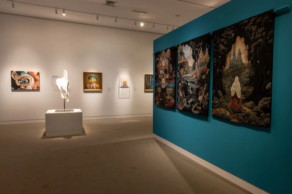 Three dark woven tapestries hang on a turquoise wall, with the white marble ear sculpture and paintings across the room.