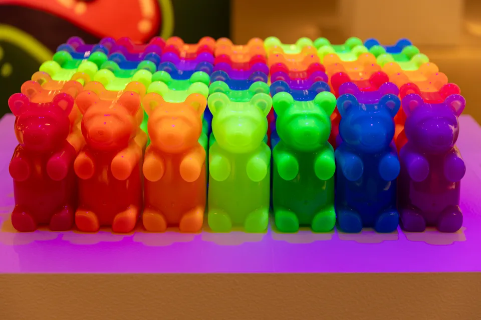Seven rows of translucent bears glow in rainbow colors on a purple-lit plinth.