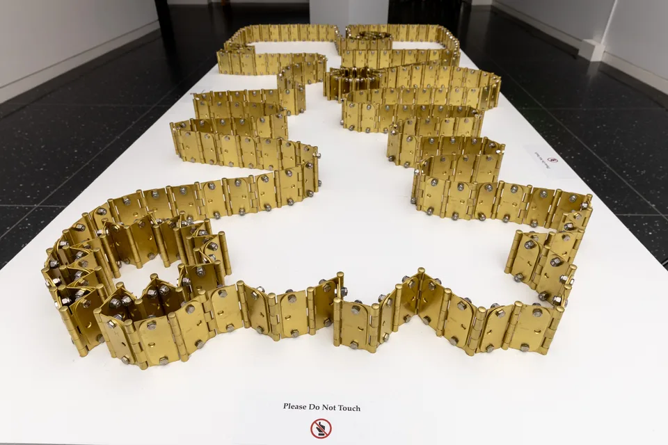 Closer view along the winding brass hinge chains on a white plinth.